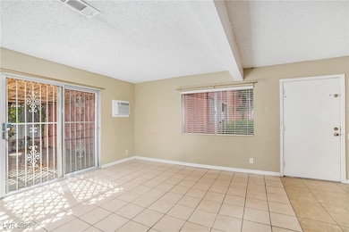 Empty room with beam ceiling, a textured ceiling, light tile patterned flooring, and a wall unit AC