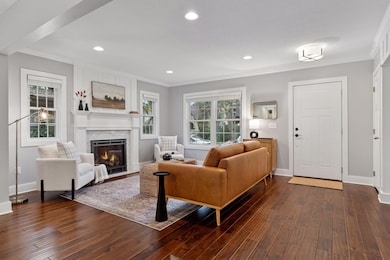 A centered fireplace framed by windows and hand-scraped wood floors create symmetry and warmth. Power and coax are prewired behind the artwork, allowing for a seamless TV setup.