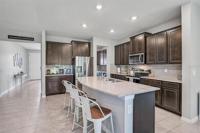This spacious kitchen features rich espresso cabinetry, sleek quartz countertops, and a stylish subway tile backsplash. The oversized island includes a dual sink and breakfast bar seating, perfect for casual dining or entertaining. Stainless steel appliances and ample storage complete the design, while the open layout flows effortlessly into the adjacent living areas.
