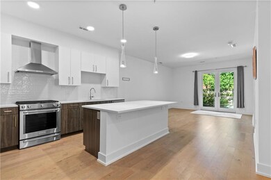 Kitchen featuring wall chimney exhaust hood, stainless steel range with gas cooktop, light countertops, a sink, and white cabinets