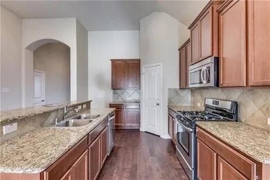 Kitchen with light stone countertops, dark hardwood / wood-style flooring, appliances with stainless steel finishes, backsplash, and sink