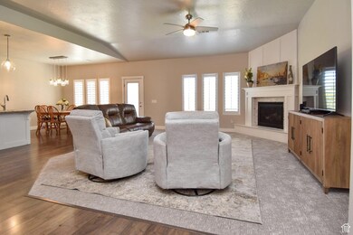 Living room with light wood-type flooring, a fireplace with raised hearth, baseboards, and ceiling fan with notable chandelier