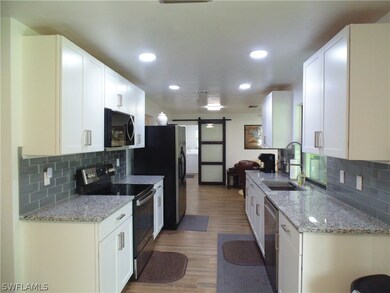 Kitchen with light wood-type flooring, stainless steel appliances, white cabinets, a barn door, and tasteful backsplash