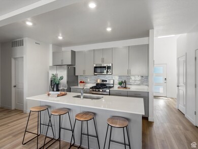 Kitchen with gray cabinetry, appliances with stainless steel finishes, a breakfast bar area, light wood-style flooring, and recessed lighting