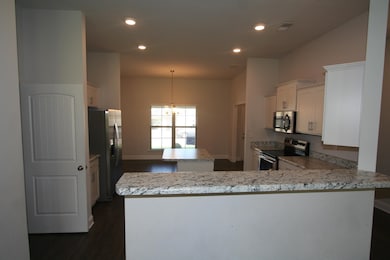 Kitchen with appliances with stainless steel finishes, a center island, a peninsula, dark wood-style floors, and a chandelier