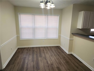 Unfurnished dining area featuring dark wood-style flooring, a chandelier, and baseboards