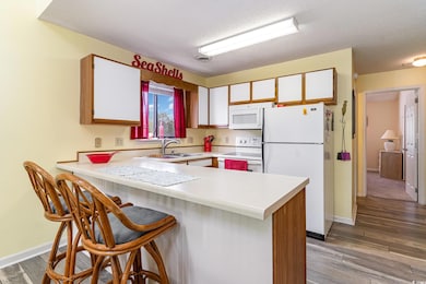 Kitchen with brown cabinetry, light countertops, a peninsula, white appliances, and a textured ceiling