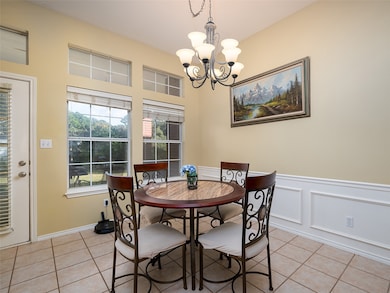 Dining room with light tile patterned flooring, wainscoting, a decorative wall, and a chandelier
