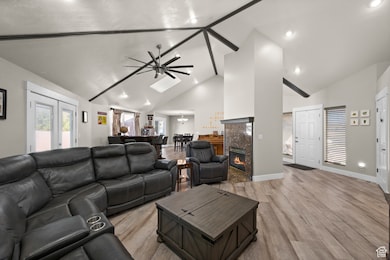 Living area featuring high vaulted ceiling, light wood-style flooring, a premium fireplace, a ceiling fan, and a skylight