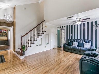 Living room featuring light wood finished floors, a chandelier, ceiling fan, and stairway