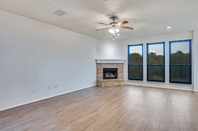 Unfurnished living room with a brick fireplace, ceiling fan, light wood-style floors, and a textured ceiling