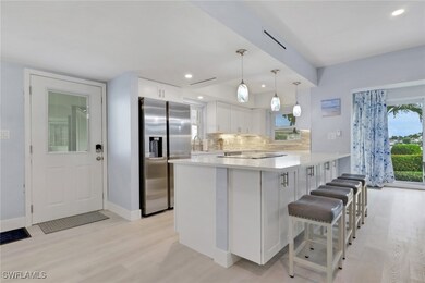 Kitchen with a peninsula, white cabinetry, stainless steel fridge with ice dispenser, decorative light fixtures, and light stone countertops