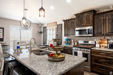 Kitchen with stainless steel appliances, an island with sink, light stone countertops, dark brown cabinetry, and backsplash