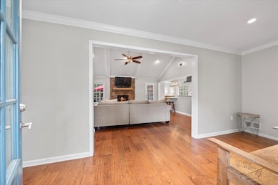 Living room featuring a fireplace, wood finished floors, a ceiling fan, baseboards, and vaulted ceiling