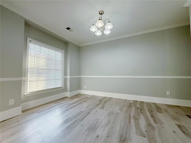 Empty room with light wood-style floors, ornamental molding, and a chandelier