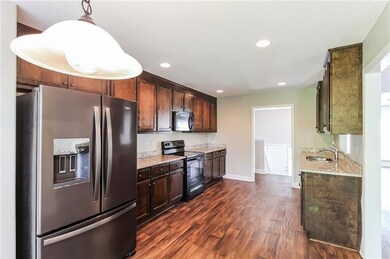 Kitchen featuring appliances with stainless steel finishes, dark wood-style flooring, light stone counters, recessed lighting, and dark brown cabinets