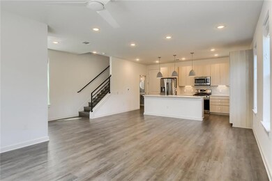 Kitchen with open floor plan, hanging light fixtures, a kitchen island with sink, stainless steel appliances, and light countertops