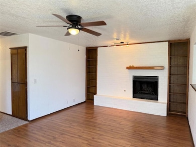 Unfurnished living room with a textured ceiling, a ceiling fan, wood finished floors, and a brick fireplace