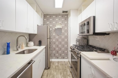 Kitchen with stainless steel appliances, backsplash, and white cabinetry