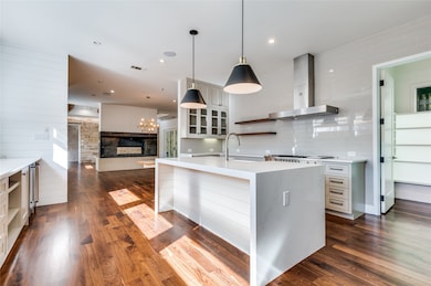 Kitchen featuring open shelves, decorative light fixtures, wall chimney range hood, dark wood-type flooring, and light stone counters