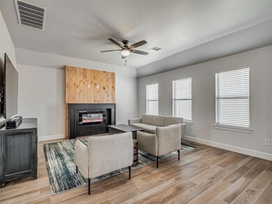 Living area with light wood-style flooring, ceiling fan, and a glass covered fireplace