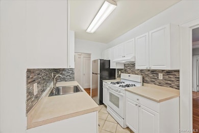 Kitchen featuring white range with gas stovetop, white cabinetry, light countertops, light tile patterned floors, and under cabinet range hood