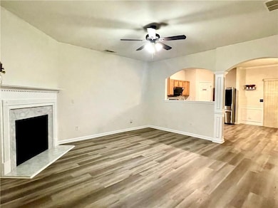 Unfurnished living room with a ceiling fan, a premium fireplace, wood finished floors, and arched walkways