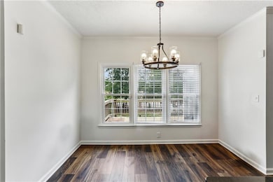 Unfurnished dining area with a chandelier, dark wood-style flooring, baseboards, a textured ceiling, and ornamental molding