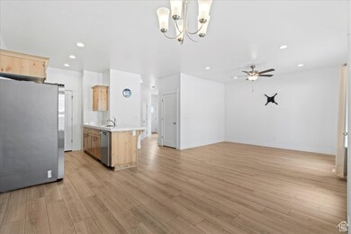 Kitchen featuring light brown cabinetry, stainless steel appliances, light countertops, open floor plan, and a chandelier