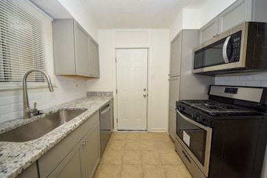 Kitchen with appliances with stainless steel finishes, gray cabinetry, backsplash, light stone countertops, and a textured ceiling
