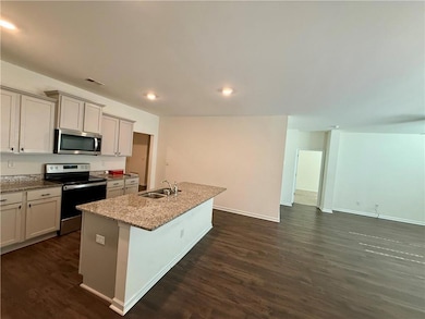 Kitchen with appliances with stainless steel finishes, light stone counters, dark wood finished floors, a center island with sink, and recessed lighting
