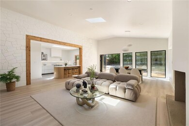 Corridor featuring light wood finished floors, a skylight, arched walkways, and high vaulted ceiling