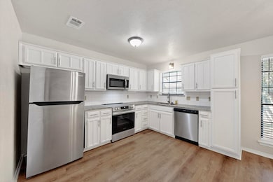 Kitchen featuring stainless steel appliances, decorative backsplash, white cabinets, light wood-type flooring, and a textured ceiling