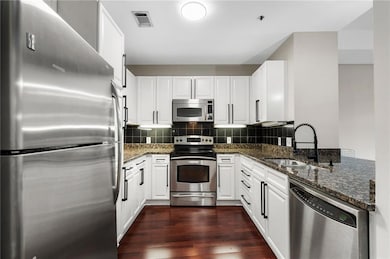 Kitchen with appliances with stainless steel finishes, a sink, dark wood-style floors, and dark stone counters