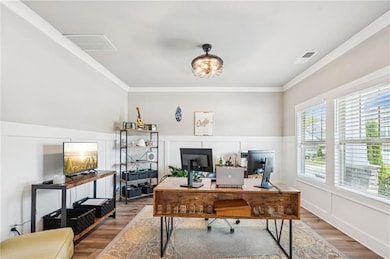 Office area featuring wood finished floors, crown molding, a wainscoted wall, and a decorative wall