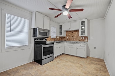 Kitchen featuring white cabinets, stainless steel appliances, ceiling fan, glass insert cabinets, and wooden walls