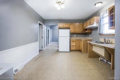 Kitchen with light countertops, freestanding refrigerator, light floors, under cabinet range hood, and brown cabinetry