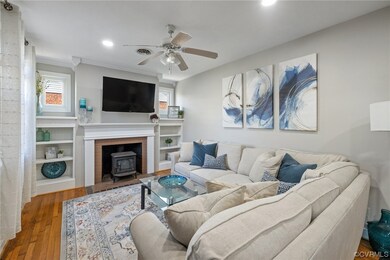 Living room with ceiling fan, a wood stove, hardwood flooring, ornamental molding, and a fireplace