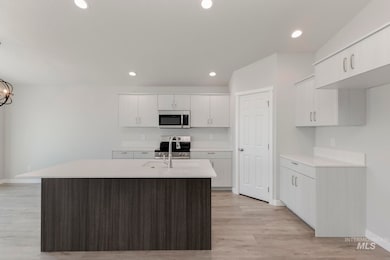 Kitchen featuring light wood finished floors, appliances with stainless steel finishes, a center island with sink, recessed lighting, and light stone countertops