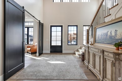 Foyer featuring a barn door, stairs, light wood-type flooring, and a towering ceiling