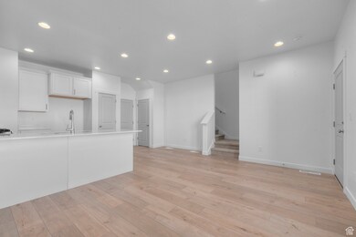 Kitchen with recessed lighting, light wood-type flooring, light countertops, white cabinets, and a sink