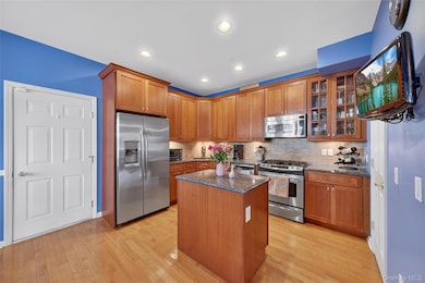 Kitchen with stainless steel appliances, granite counters, a kitchen island, glass insert cabinets, and wood flooring