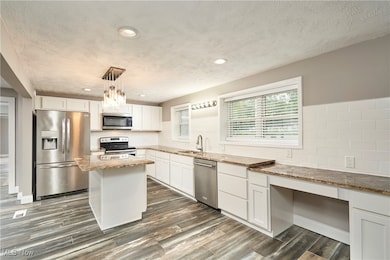 Kitchen with appliances with stainless steel finishes, white cabinetry, light stone counters, recessed lighting, and a center island