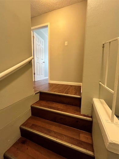 Stairs with a textured wall, a textured ceiling, and wood finished floors