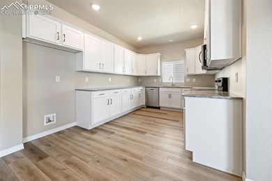 Kitchen with stainless steel appliances, light wood-style flooring, light stone counters, white cabinetry, and recessed lighting