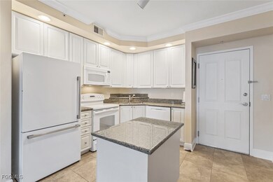 Kitchen with white appliances, white cabinets, dark stone countertops, ornamental molding, and light tile patterned floors
