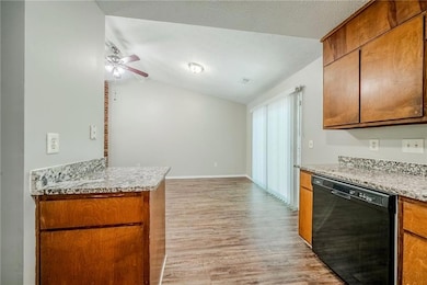 Kitchen with dishwasher, light wood-style floors, vaulted ceiling, brown cabinets, and ceiling fan