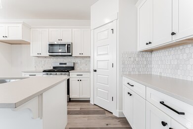Kitchen featuring appliances with stainless steel finishes, light countertops, light wood-style flooring, white cabinetry, and decorative backsplash