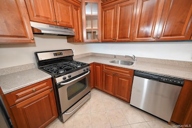 Kitchen featuring stainless steel appliances, light stone counters, under cabinet range hood, and light tile patterned flooring