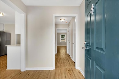 Bright and welcoming entryway featuring warm wood floors, neutral walls, and a peek into the kitchen